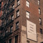 Image of the side of a apartment building like in new york with a sign that reads, "how are you really?" S4 E20 - Struggle Engaging? You Might Be Languishing Or Dormant